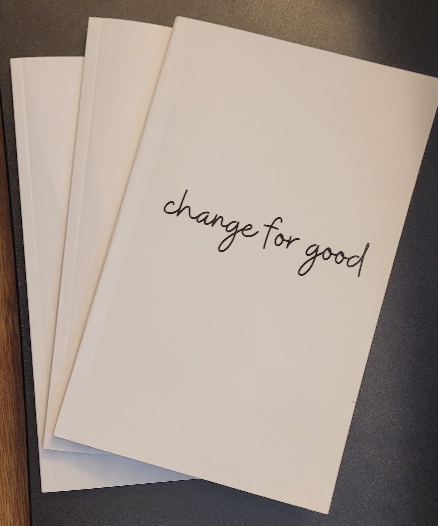 Three white notebooks on a dark background, the top one shows a simple script font saying “change for good”